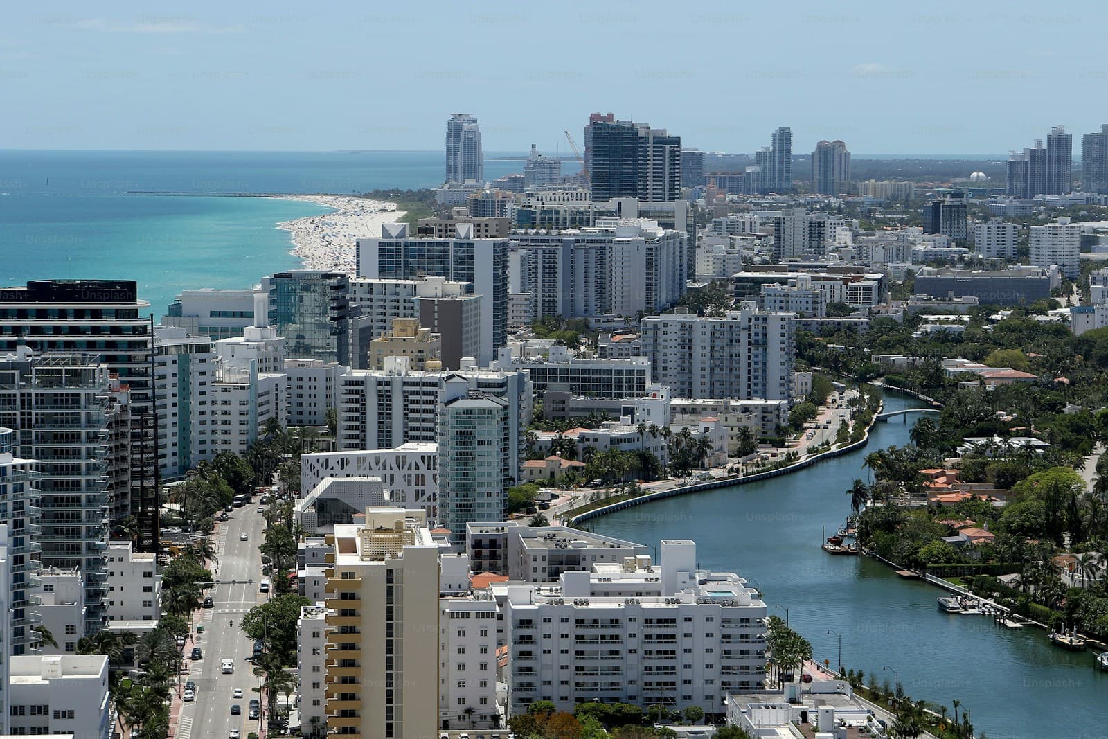 Aerial view of coastal city with high-rise buildings, beach, and waterway running through urban development