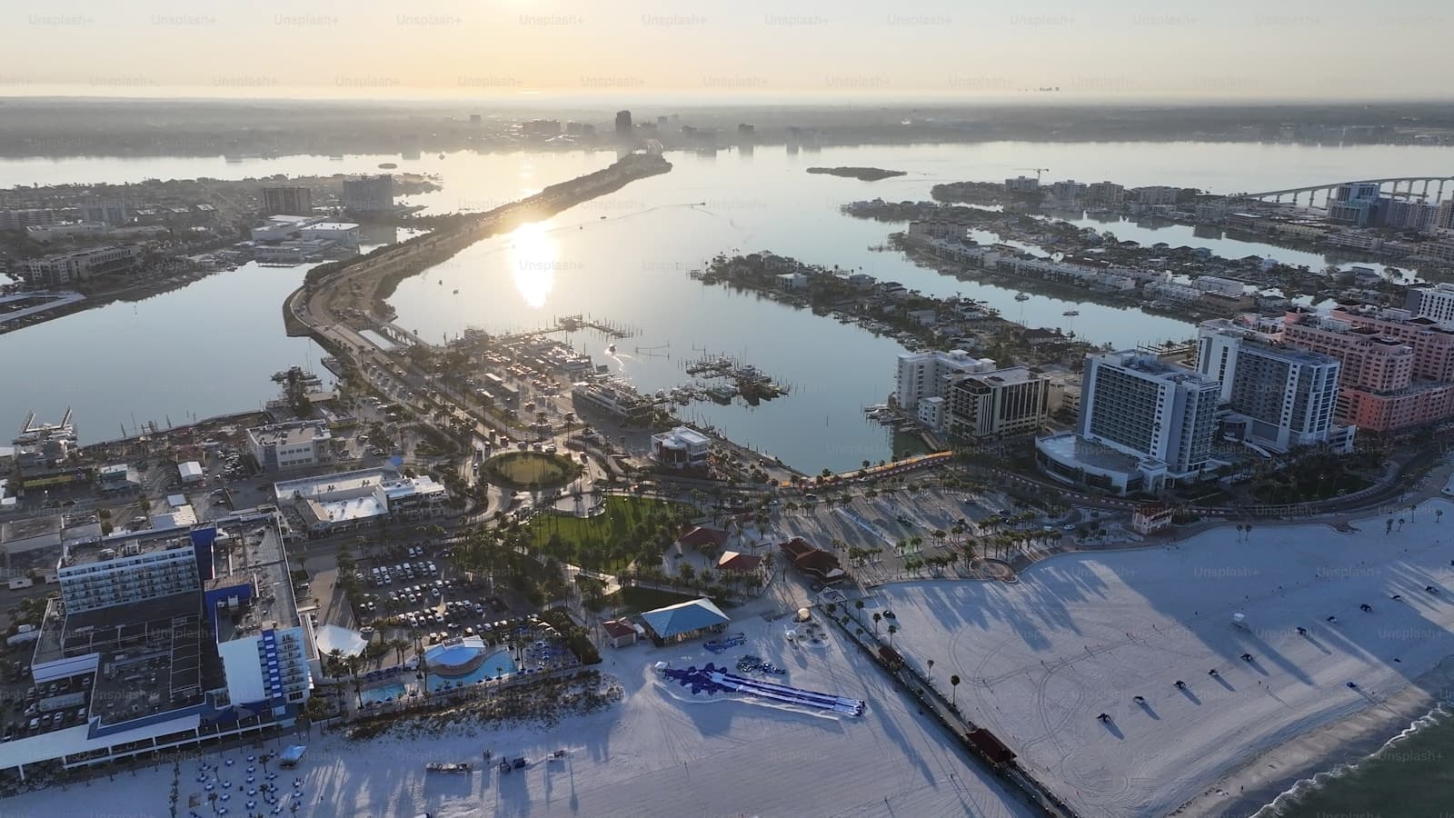 Aerial sunset view of coastal city with curved bridge, waterfront buildings and golden water reflections