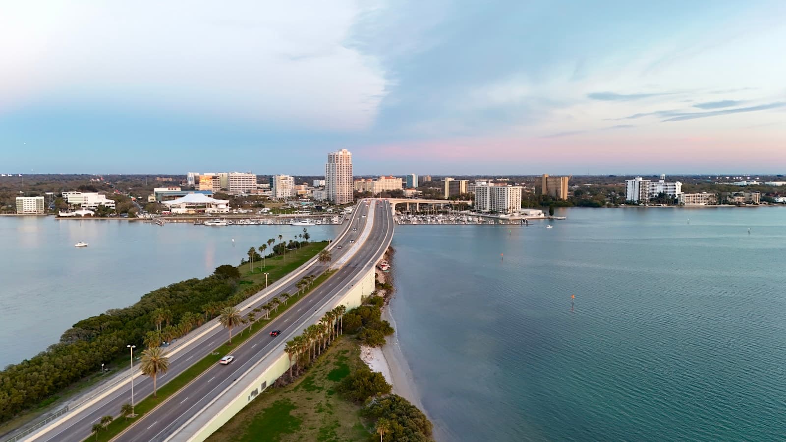 Aerial view of causeway bridge crossing water to connect with city skyline and high-rise buildings