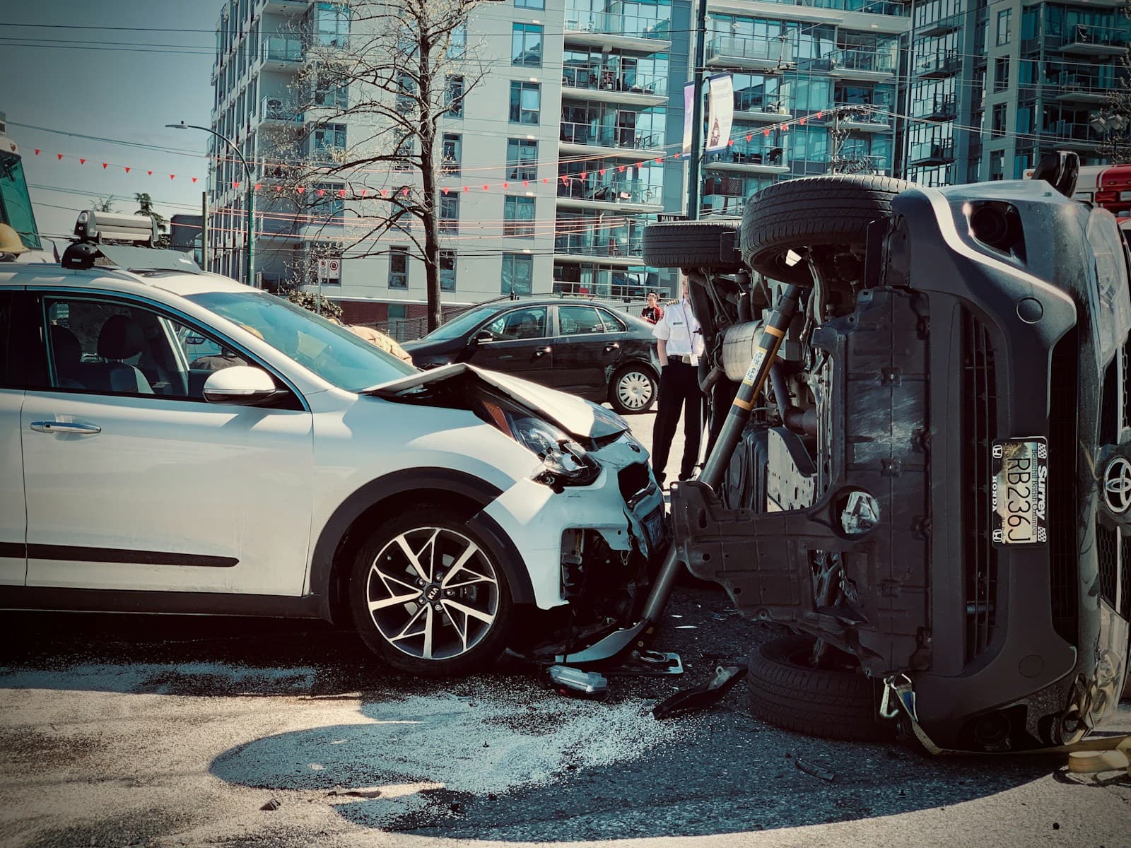 Traffic accident with white car and overturned dark SUV on city street with apartment buildings in background