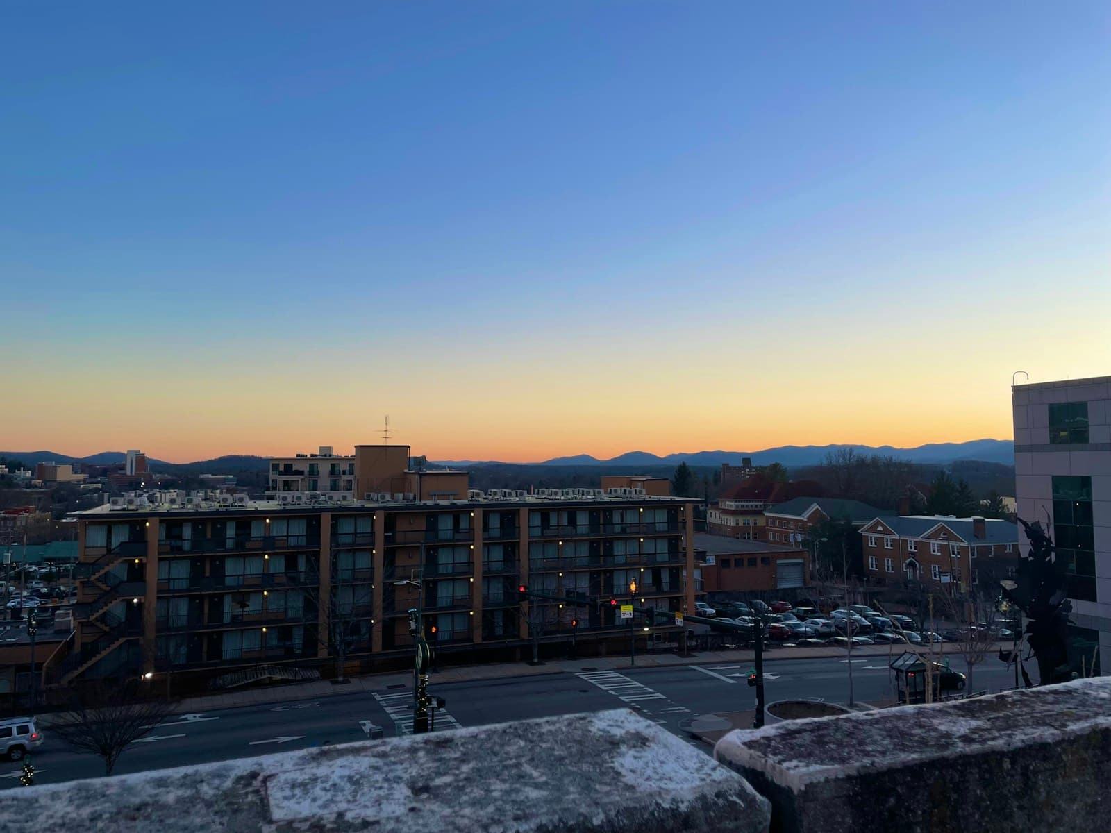 City view at sunset with apartment buildings, parking lots, and mountains in the background under a clear sky