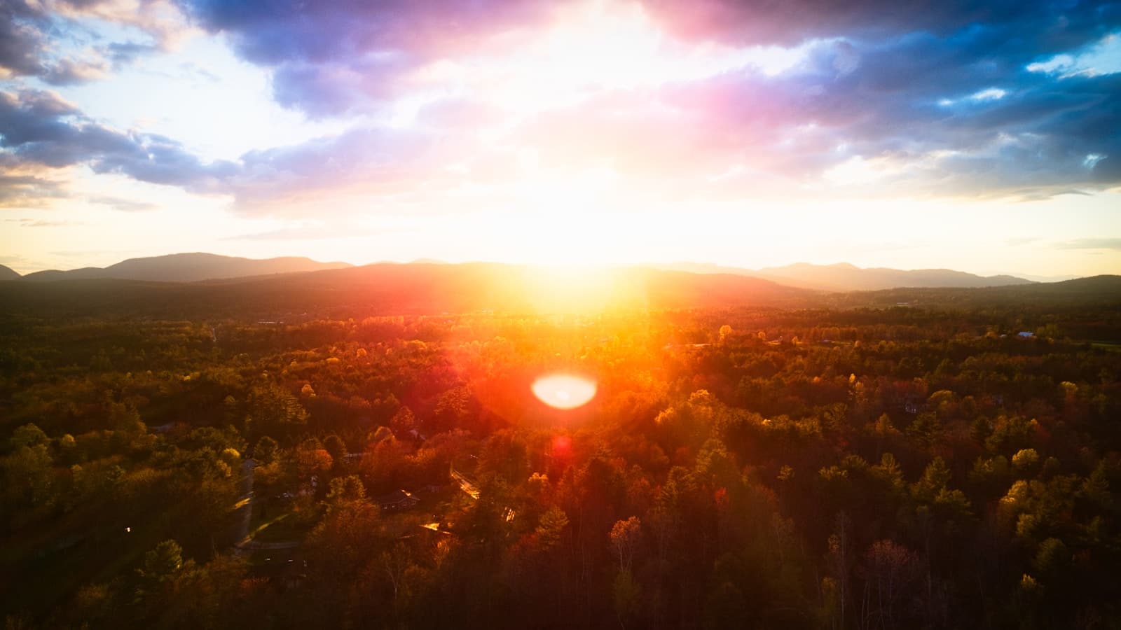 Aerial view of golden sunset over forested hills with dramatic orange and pink sky