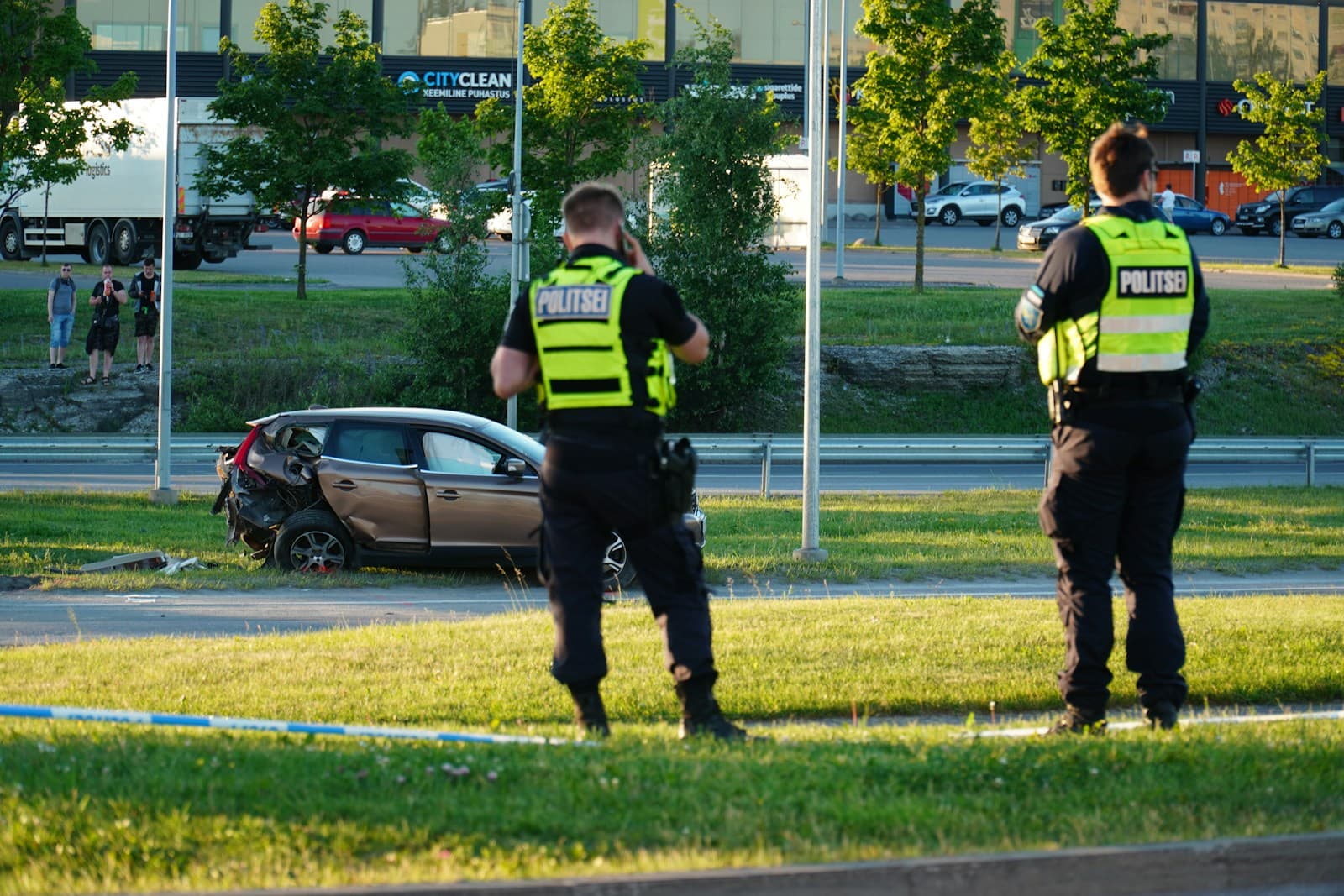 Two police officers in reflective vests at car accident scene with damaged vehicle on grass near roadway