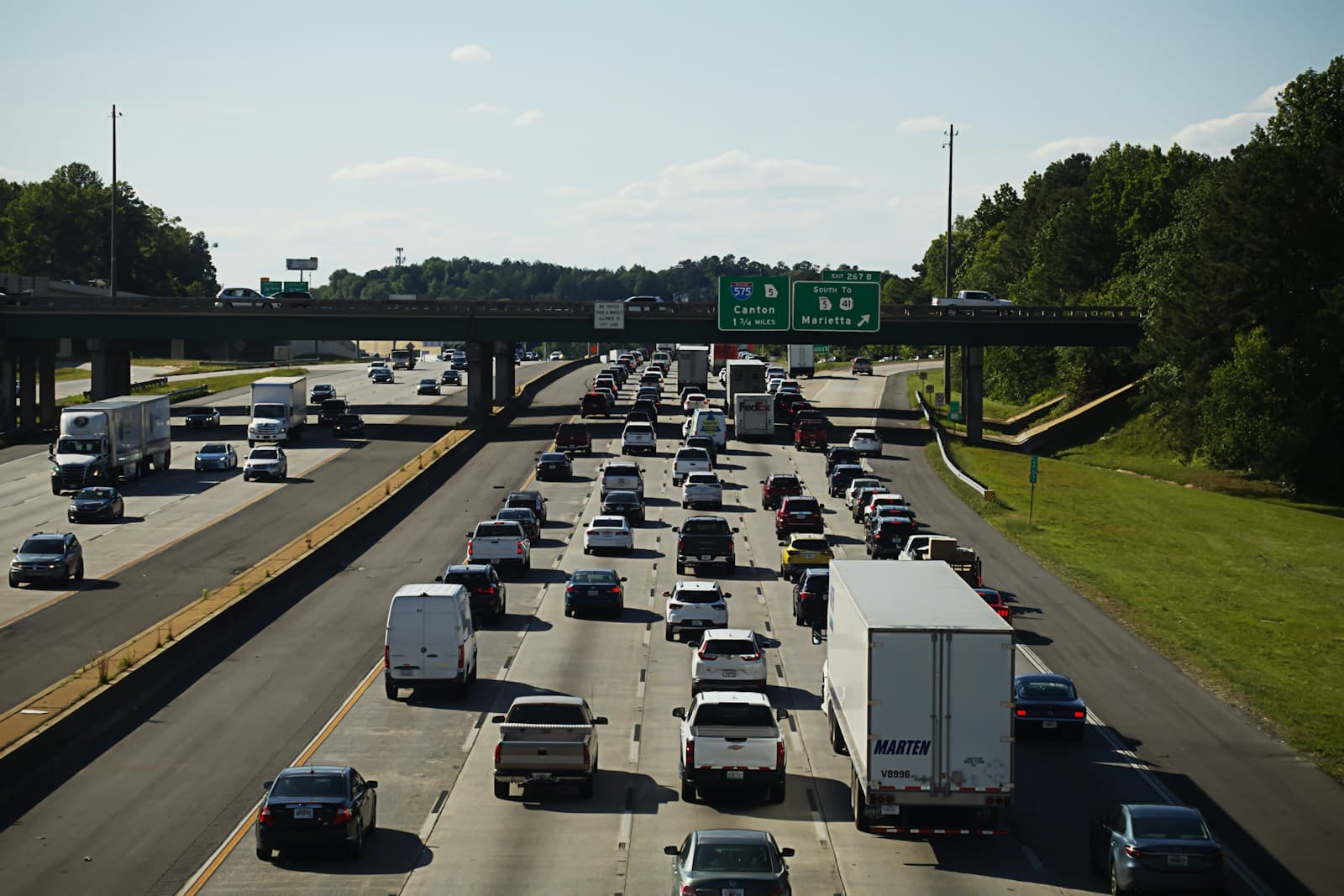 Heavy traffic on a multi-lane highway with cars and trucks, green highway signs, and trees lining both sides