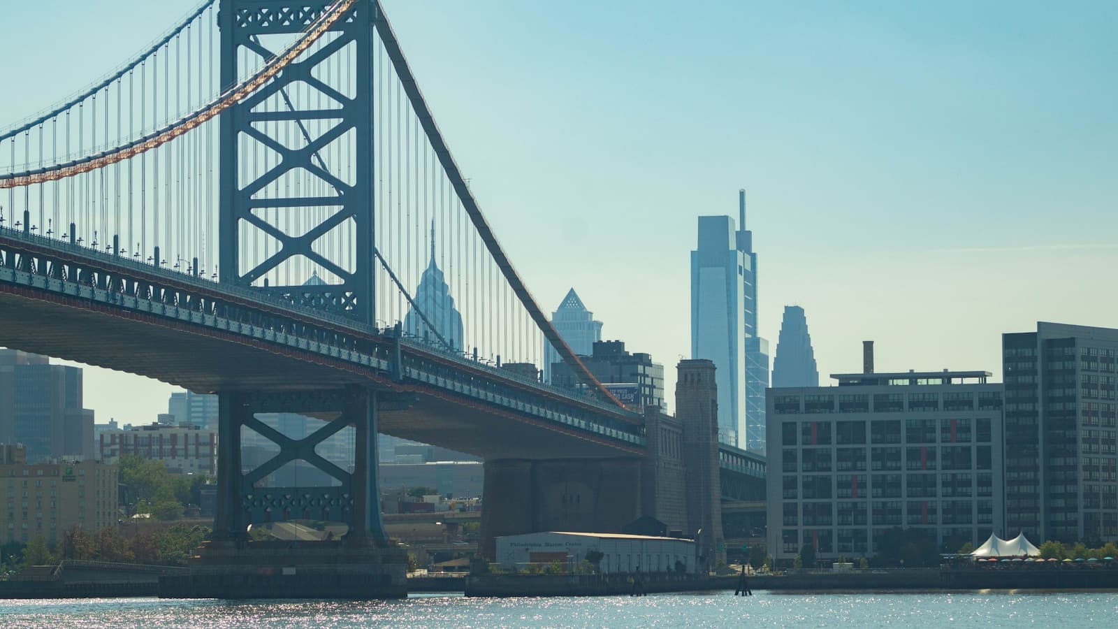 Suspension bridge over water with city skyline and tall buildings in background